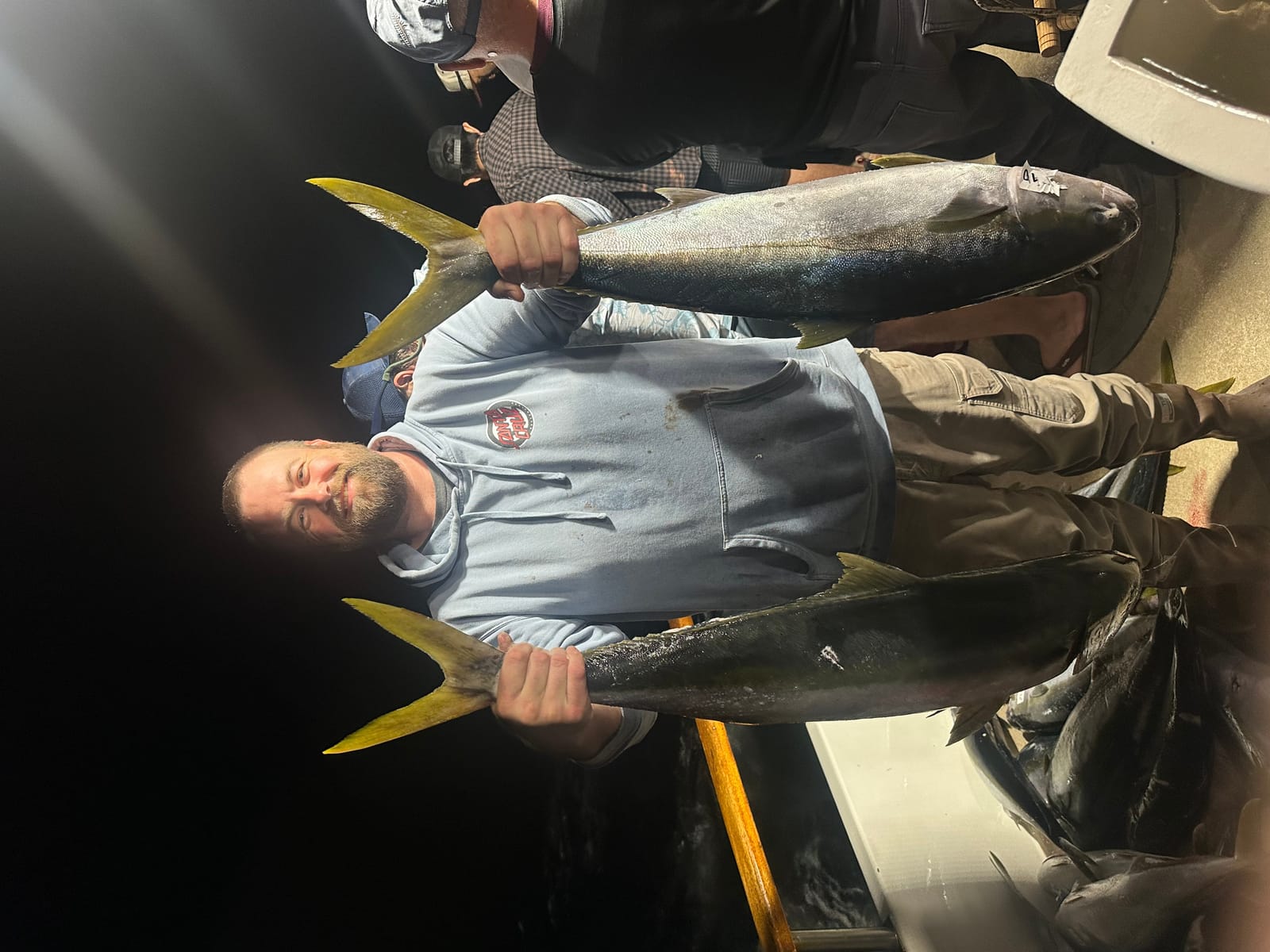 Keith Leonard holding his two yellowtail at the rail of the Horizon at night