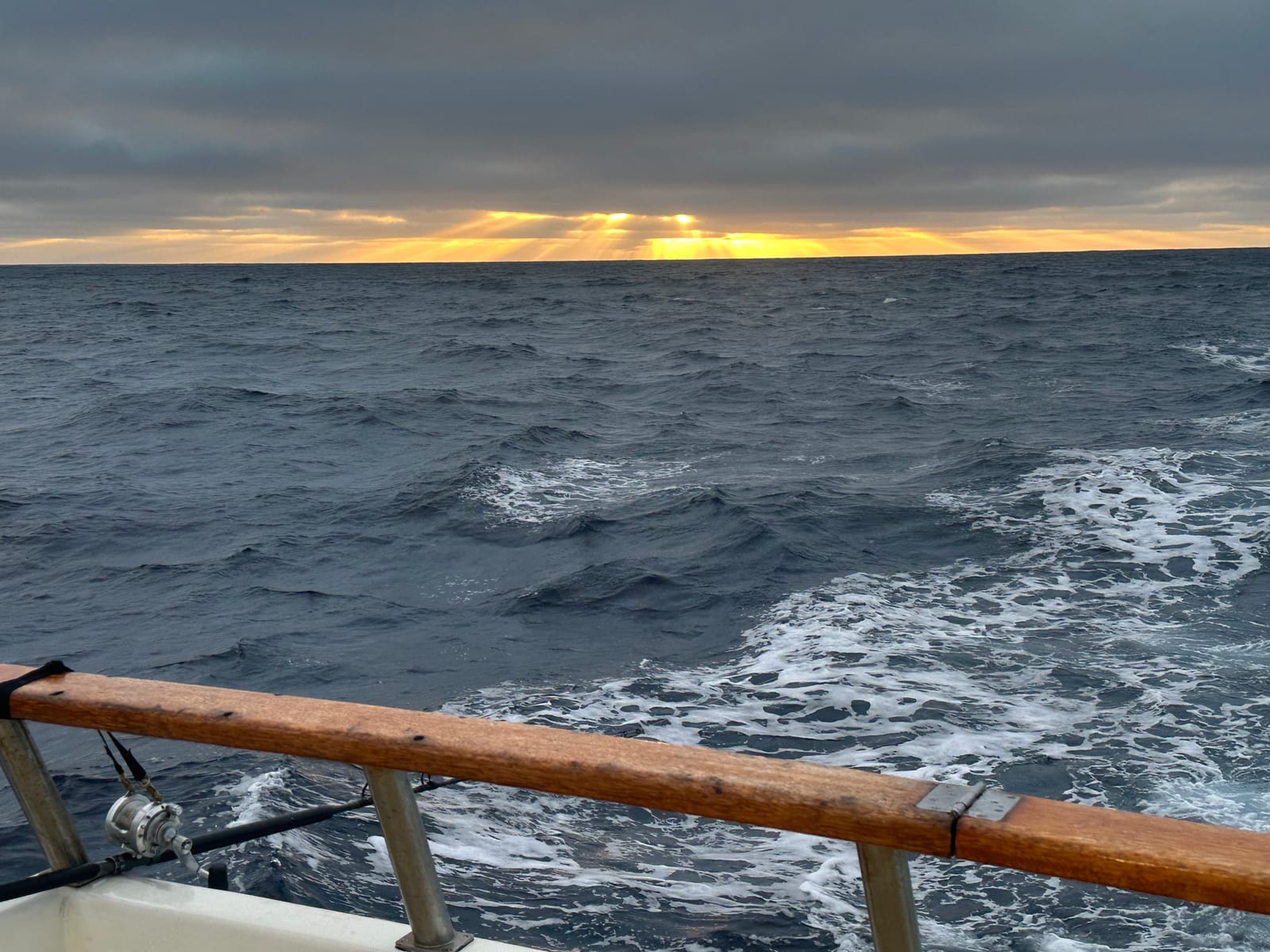 Sunrise light breaking through clouds over the open ocean behind the Horizon's wake