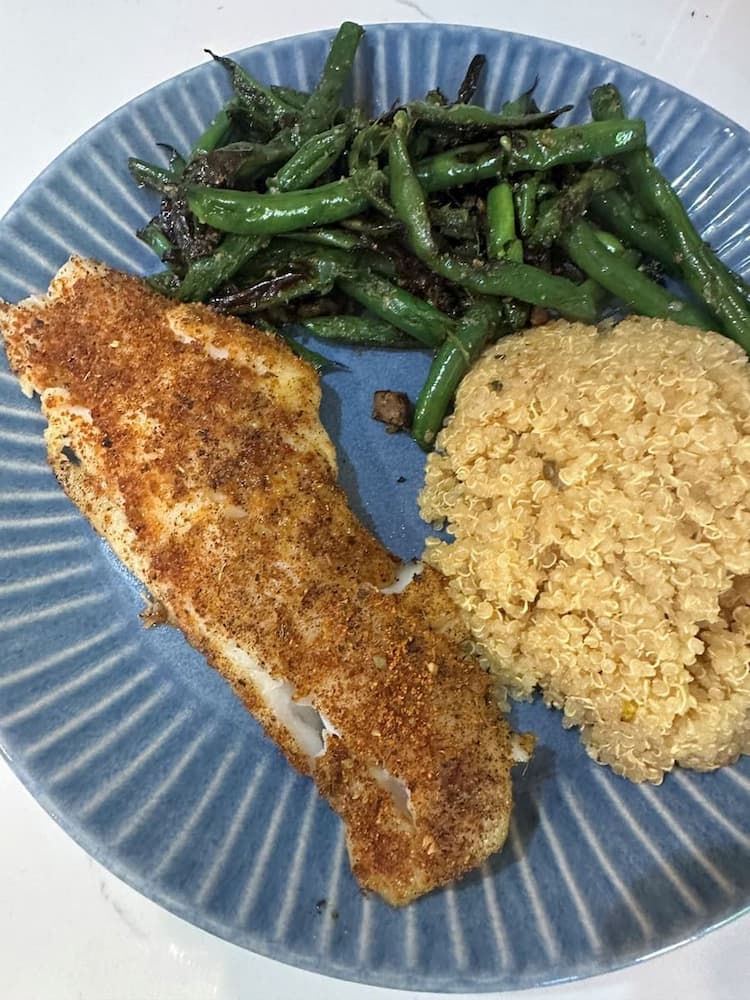 A pan-seared fish fillet with sautéed garlic green beans and quinoa on a blue plate — dinner from a recent trip